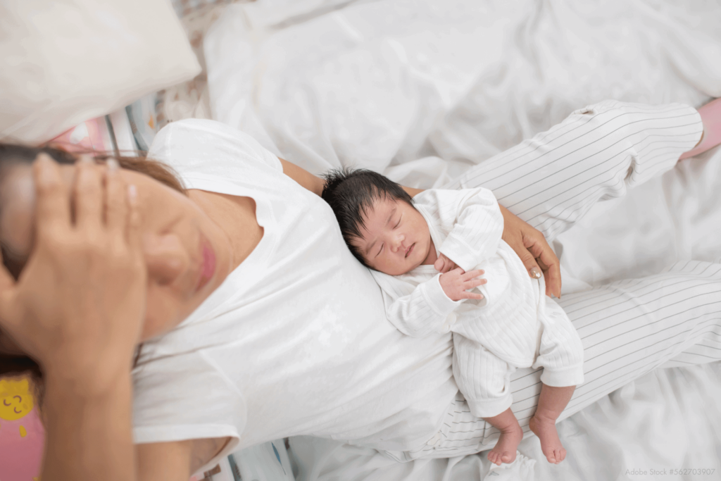 frisch gebackene mama mit neugeborenem auf dem schoß haelt sich verzweifelt die hand an die stirn gut dass sie auch jetzt sicher verhuetet mit der kupferkette gynefix