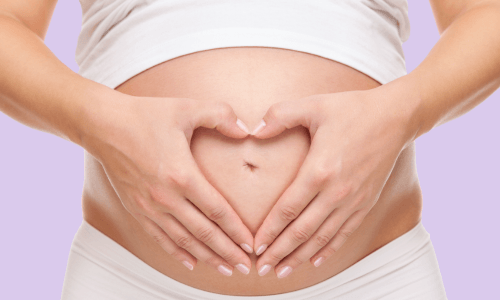 Schwanger nach Spirale, Bauch einer Schwangeren mit Händen in Herzform über dem Nabel